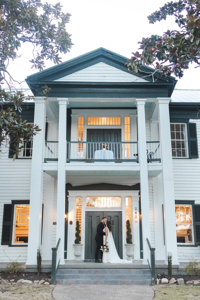 Bride and groom sharing a kiss in front of a two story building at their SC wedding venue.