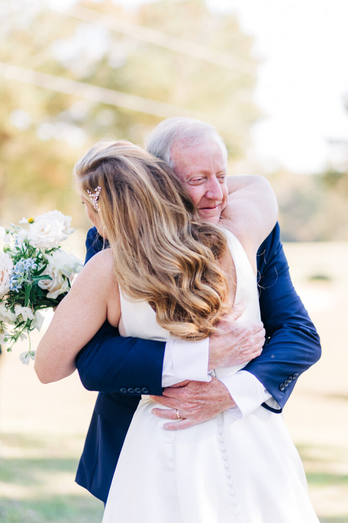 Bride holding her bouquet while hugging her father during their first look before the wedding ceremony. 