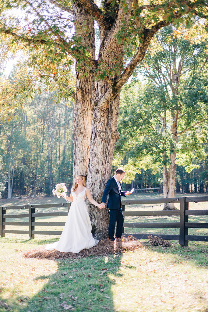 Bride and groom holding hands on either side of a tree while sharing their first touch on wedding day