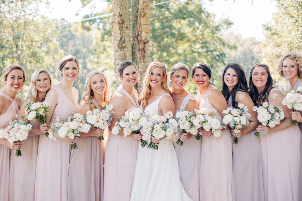 bride and bridesmaids standing together in a line while holding bouquets.