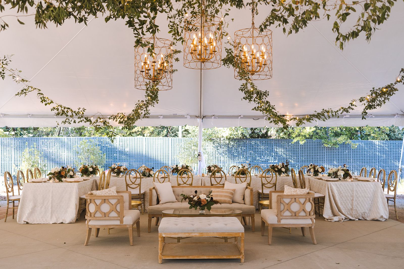 Tented wedding reception with greenery, chandeliers, and lounge.