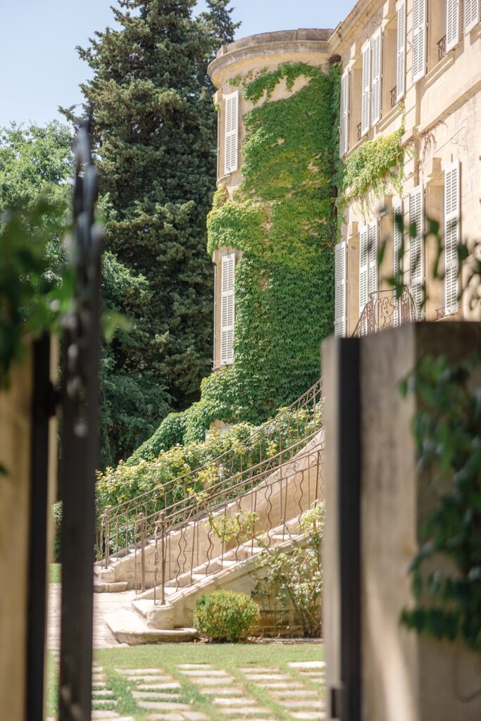 Romantic château entrance with ivy-clad stone walls, elegant shuttered windows, and graceful stairways lined with greenery
