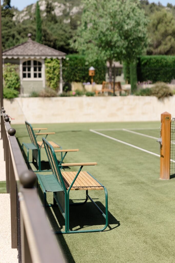 Private tennis court surrounded by lush greenery and countryside charm, complete with shaded seating for relaxation